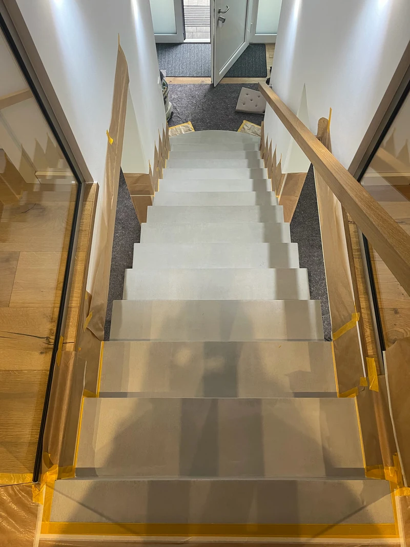 Treppe aus Beton Ciré in Marl von oben vor der Reparatur, Stufen mit Klebeband abgeklebt, Glasgeländer an der Seite