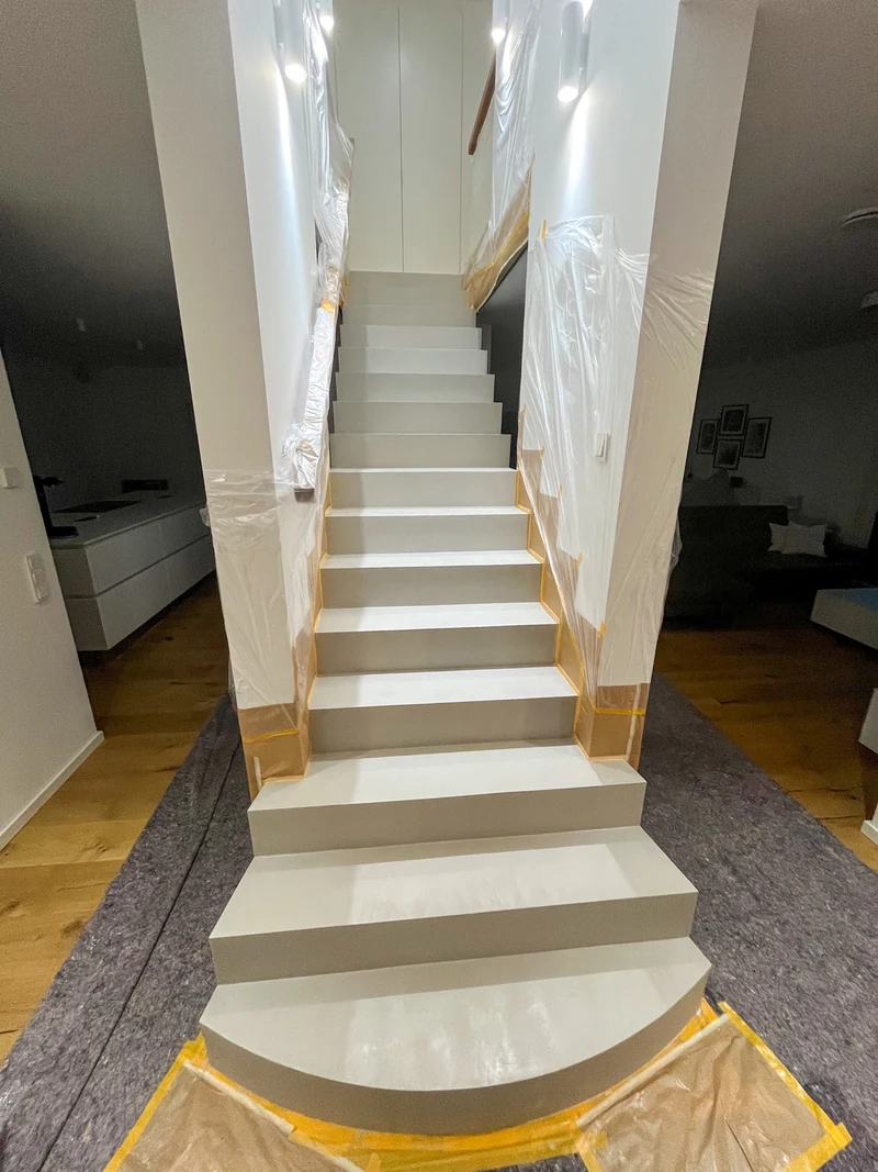 Zweite Lage Beton Ciré noch nass auf der Treppe, dunklere Flächen, Blick vom Fuß der Treppe mit Abdeckung