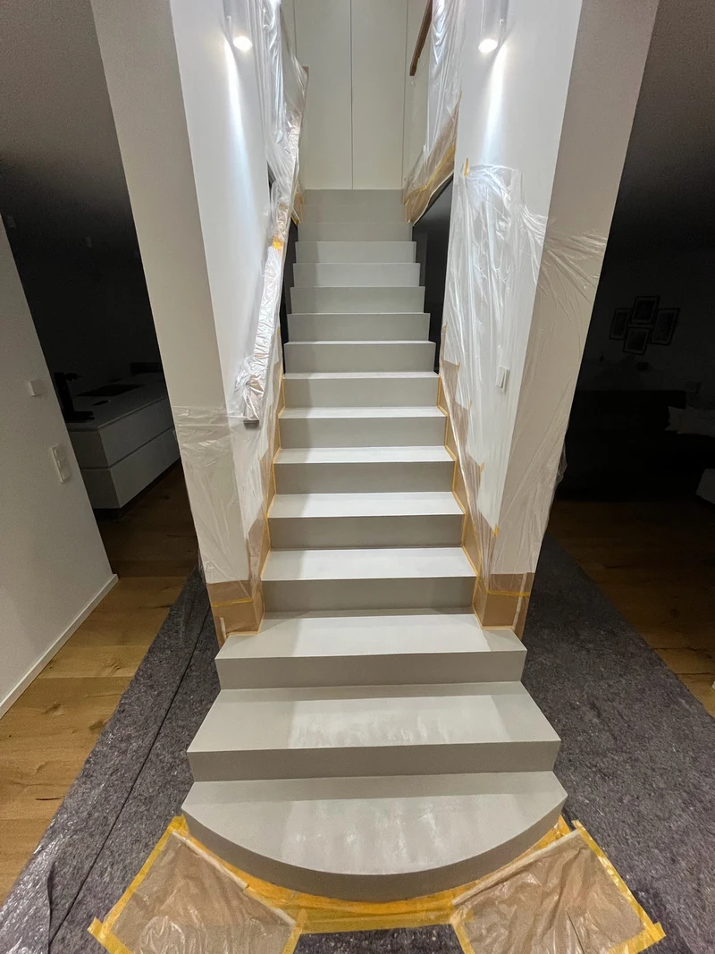Gesamtansicht der Treppe mit nasser zweiter Lage Beton Ciré, runde Antrittsstufe und Abdeckung am Boden