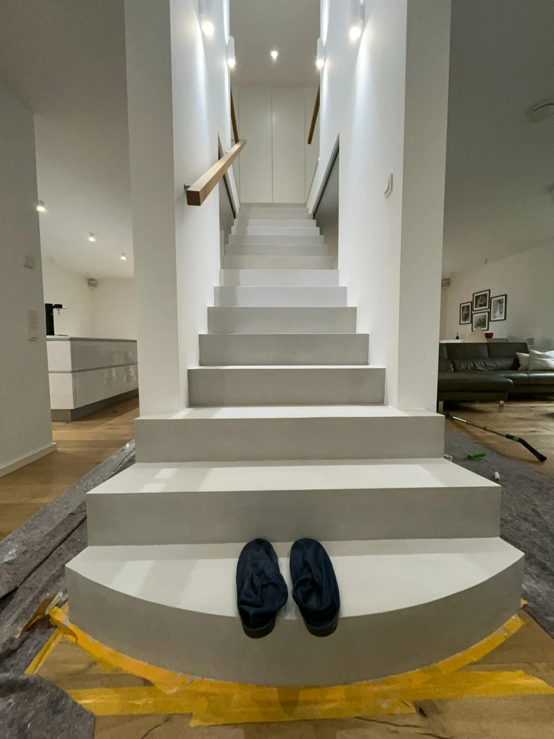 Gereinigte Treppe aus Beton Ciré, auf der runden Antrittsstufe stehen Überschuhe für das weitere Betreten