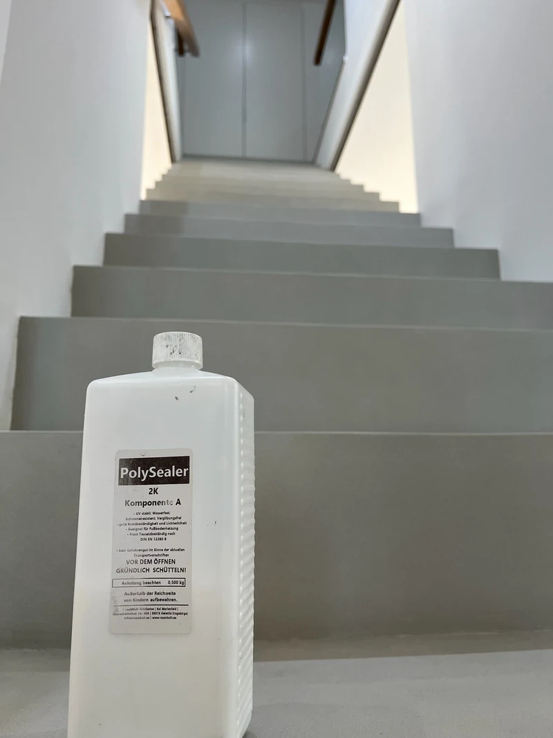 Gebinde der Versiegelung PolySealer 2K von rauMKult steht auf der reparierten Treppe aus Beton Ciré