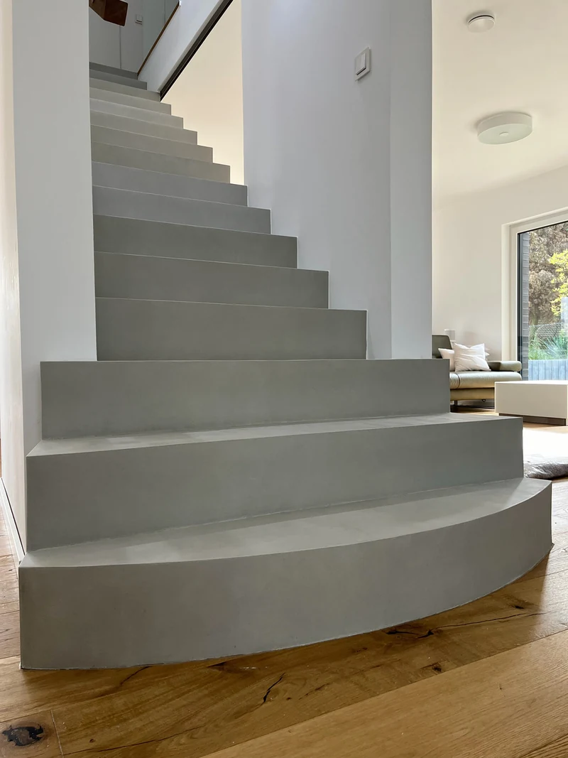 Von der runden Antrittsstufe aus Beton Ciré die Stufen hinauf, seitlicher Blick in den hellen Wohnraum