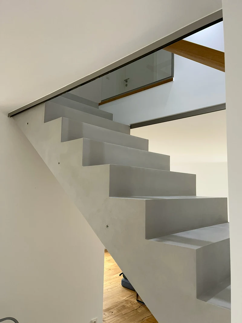Treppe aus Beton Ciré von der Seite unter dem Glasgeländer, Setzstufen und Tritte nach der Reparatur