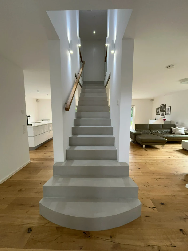 Fertig reparierte Treppe aus Beton Ciré in Marl vom Fuß aus, runde Antrittsstufe, Holzhandlauf und helle Wände