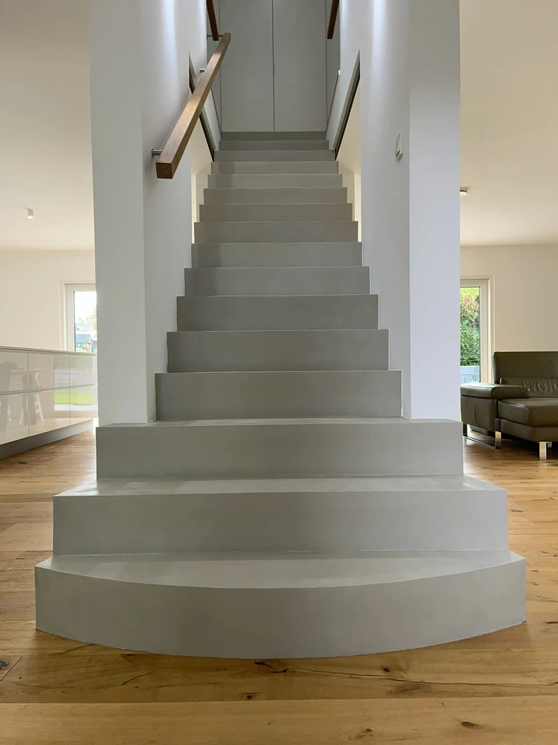 Fertige Treppe aus Beton Ciré mit Holzhandlauf und runder Antrittsstufe, Blick aus dem Wohnraum die Stufen hinauf