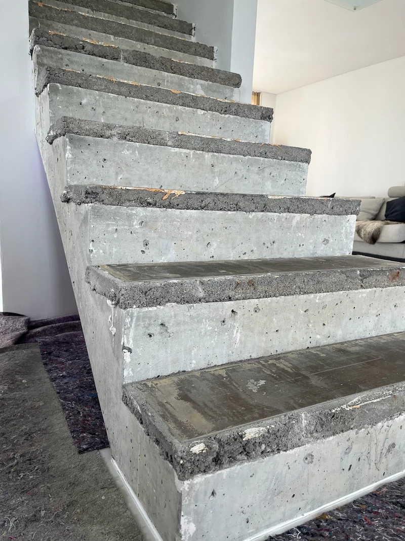 Flanke der Bestandstreppe von unten links, die aufbetonierte Erhöhung sitzt als raue Kante auf der helleren alten Stufe