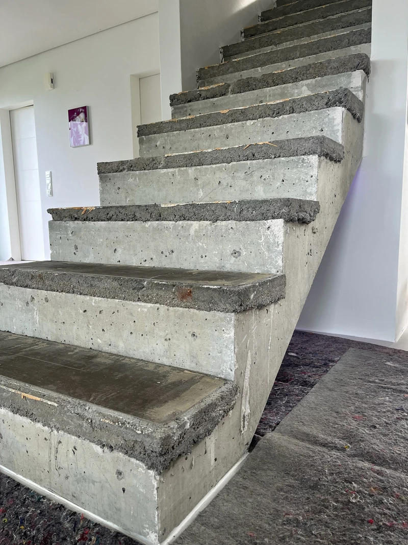 Bestandstreppe aus Beton von links vor der Beschichtung, auf den Tritten liegt eine raue, dunklere Erhöhung über den alten Stufen