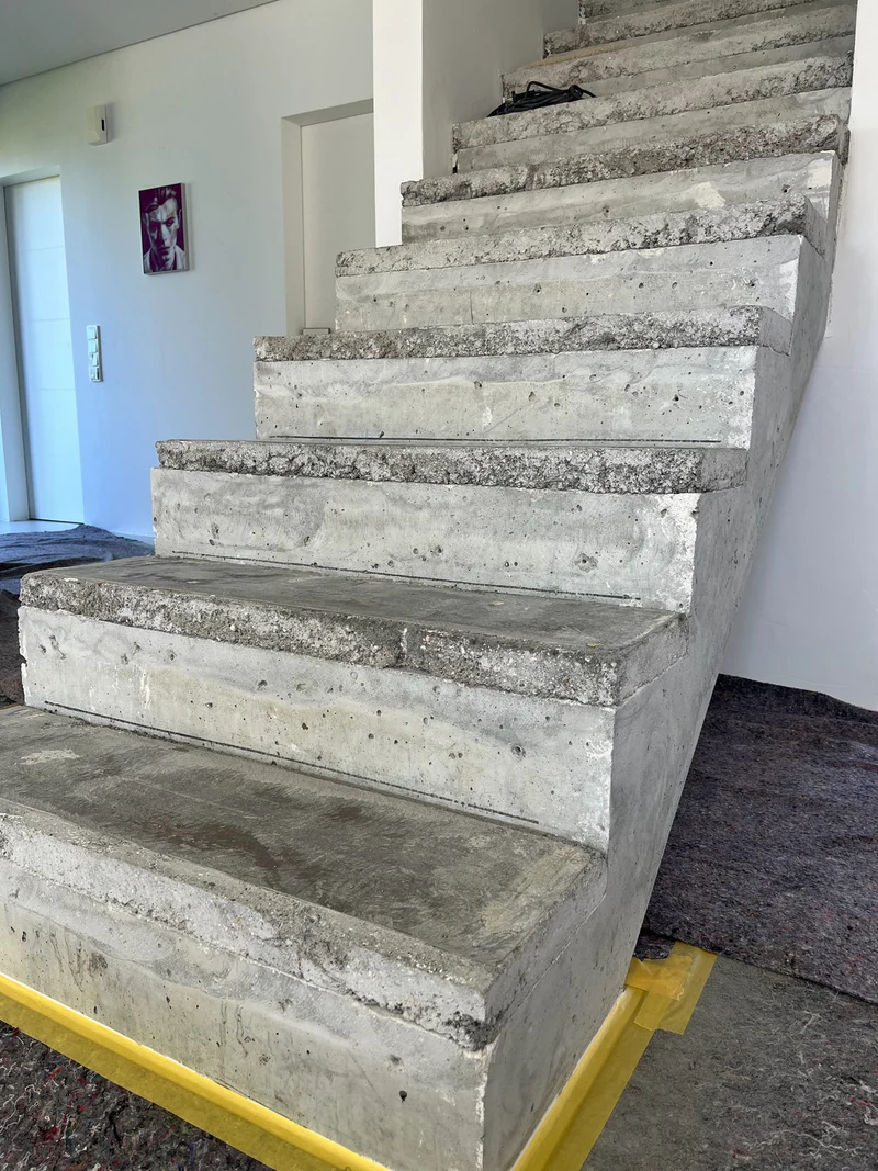 Vorher: aufbetonierte Treppe von unten links, vorspringende raue Kanten der Erhöhung, Klebeband am Antritt
