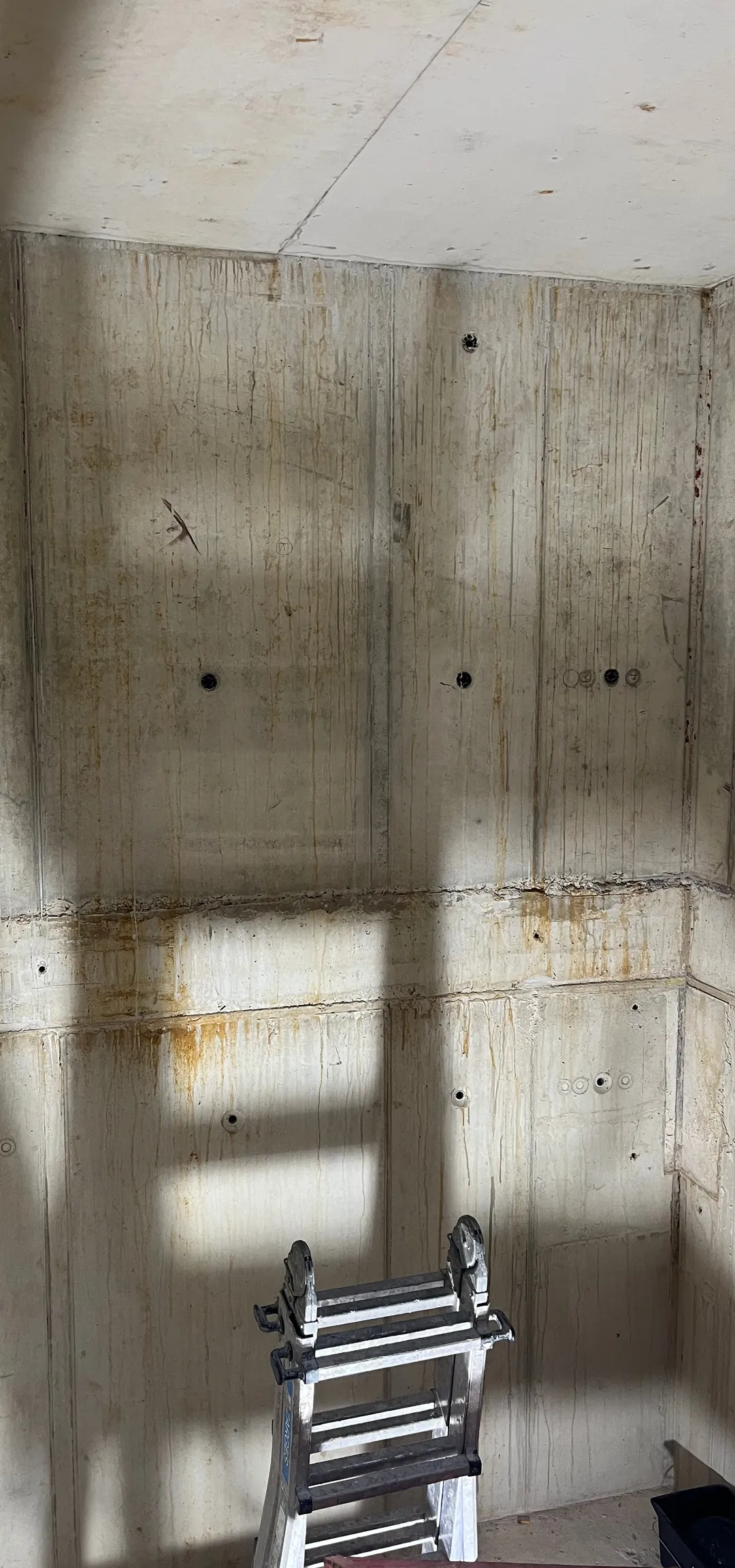 Sichtbetonwand im Treppenhaus des Wasserwerks Einsiedel vor der Betonkosmetik: offene Ankerkonen und Bohrlöcher, unruhige Schalungsübergänge am Deckenstreifen, Lichtstreifen vom Fenster